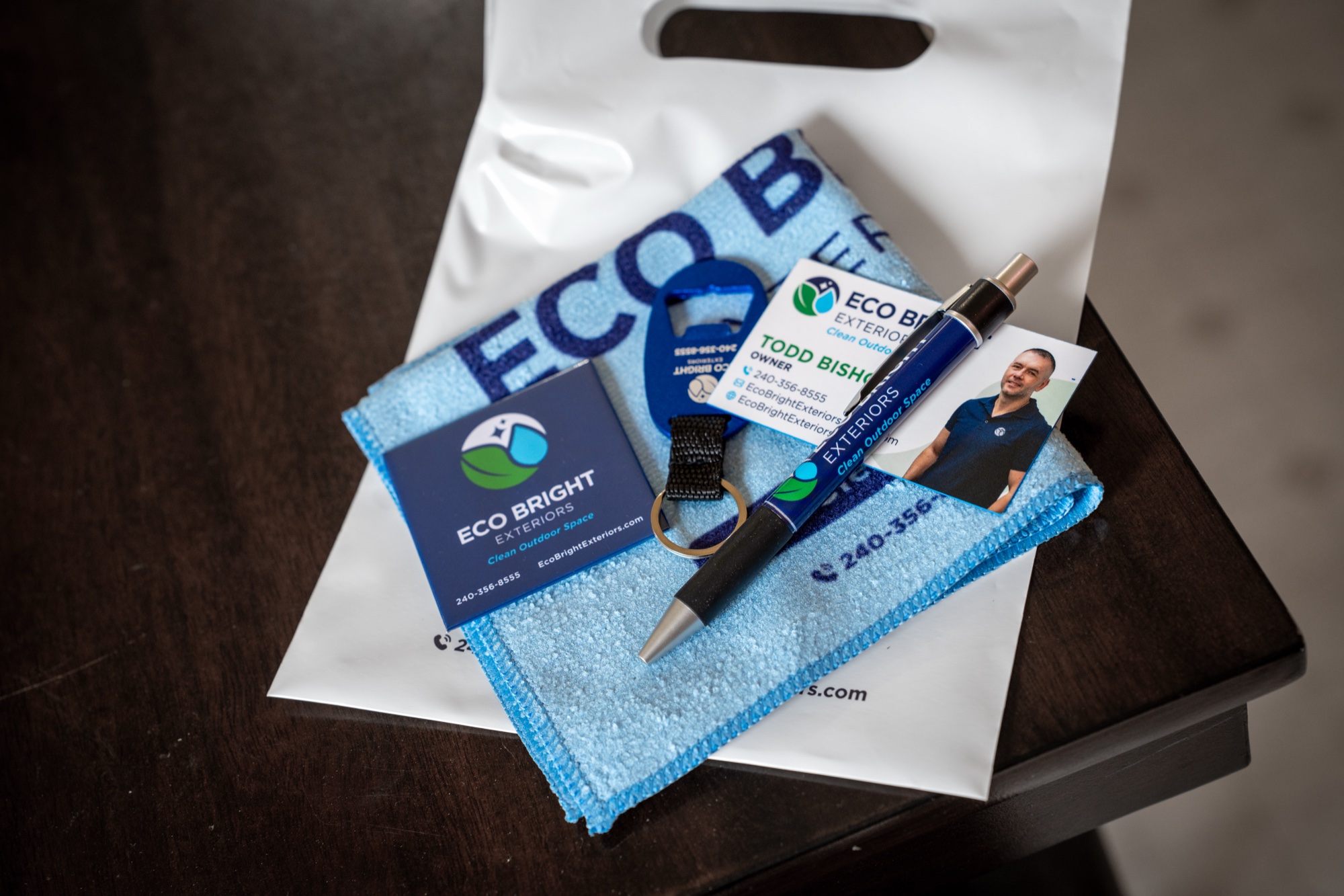Eco Bright Exteriors thank-you bag contents: custom microfiber cloth, branded pen, keychain bottle opener, fridge magnet, and business cards